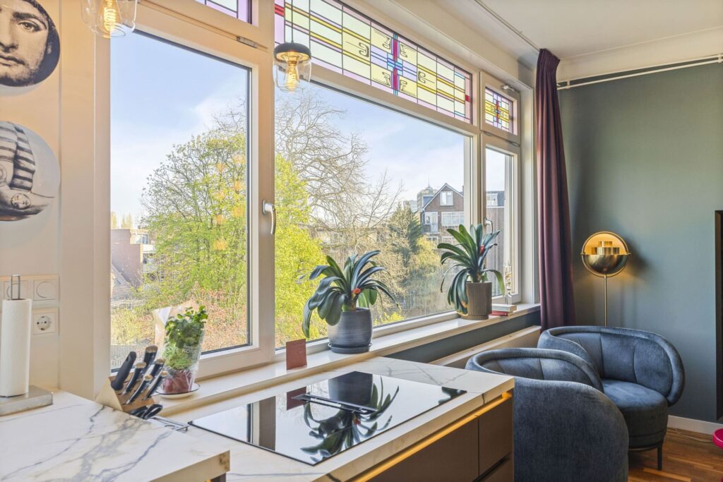 Marmerlook keukeneiland met zithoek en fluwelen stoelen bij glas-in-lood ramen