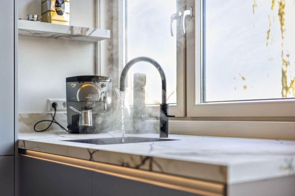 Espressomachine en keukenkraan met stromend water op marmerlook werkblad