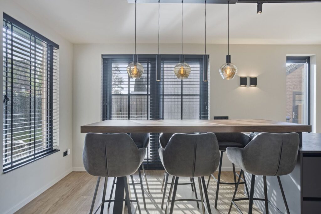 Houten bartafel met grijze fluwelen barkrukken bij raam met houten shutters
