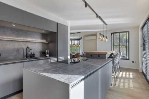 Grijze moderne keuken met groot kookeiland, inductiekookplaat en zicht op eethoek