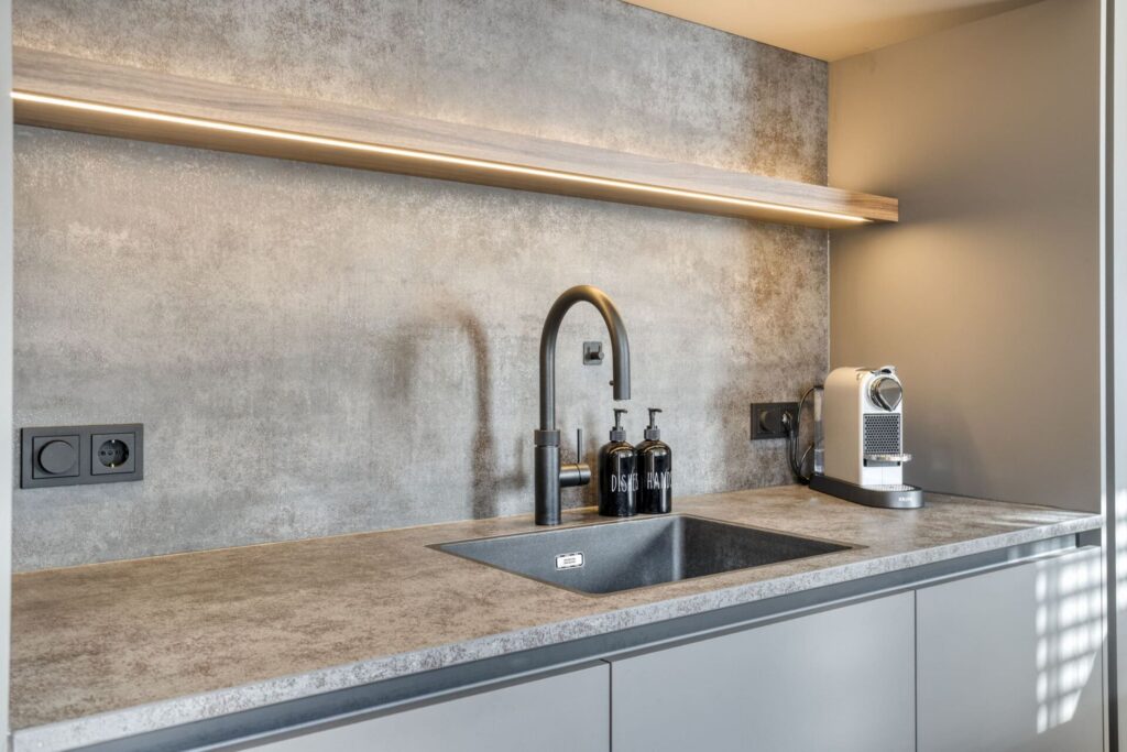 Spoelbak met kraan en verlichte wandplank in moderne keuken met betonlook achterwand